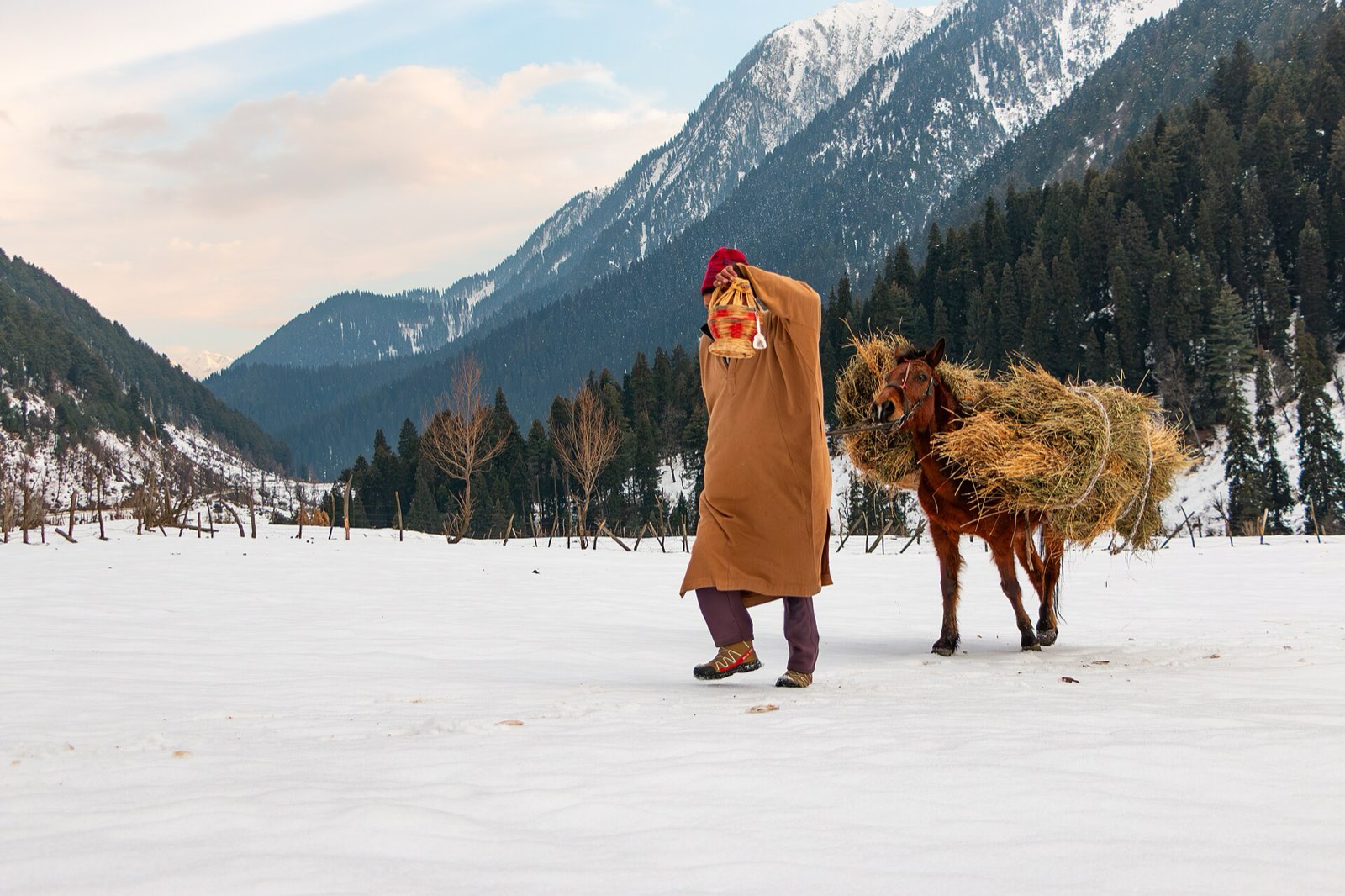 A man in a pheran leading a pony through deep snow at Aru in winter